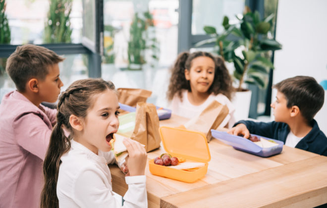 schoolkids eating healthy school lunch while sitting toget